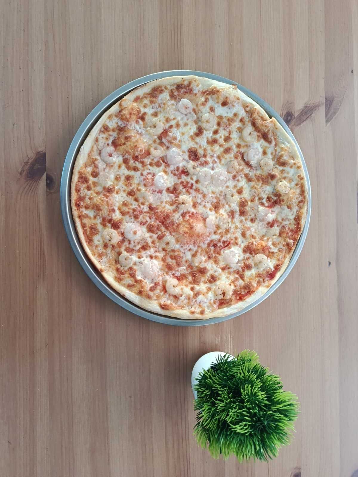 Una pizza de queso dorada sobre una bandeja de metal reposa sobre una mesa de madera.