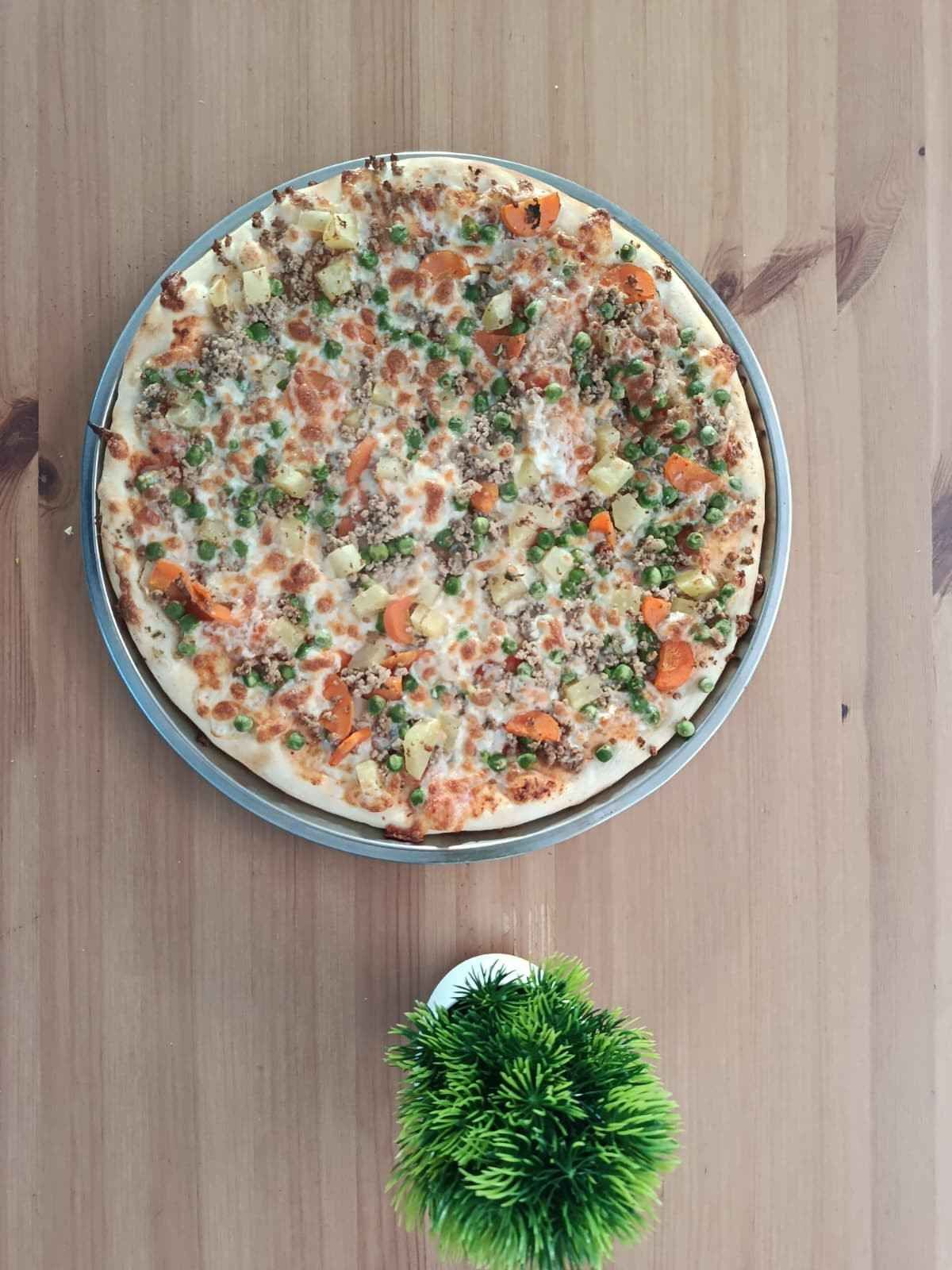 Una pizza cubierta de verduras, colocada en una bandeja de metal sobre una mesa de madera,