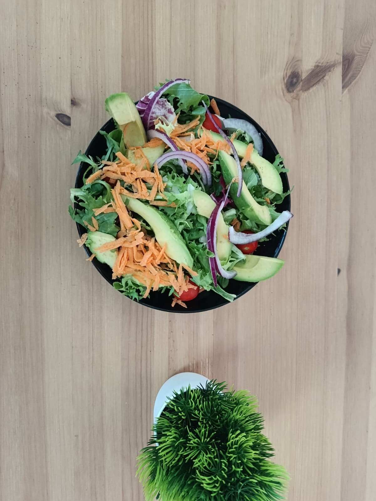 Vista desde arriba de una ensalada fresca con aguacate, zanahorias ralladas y cebolla.