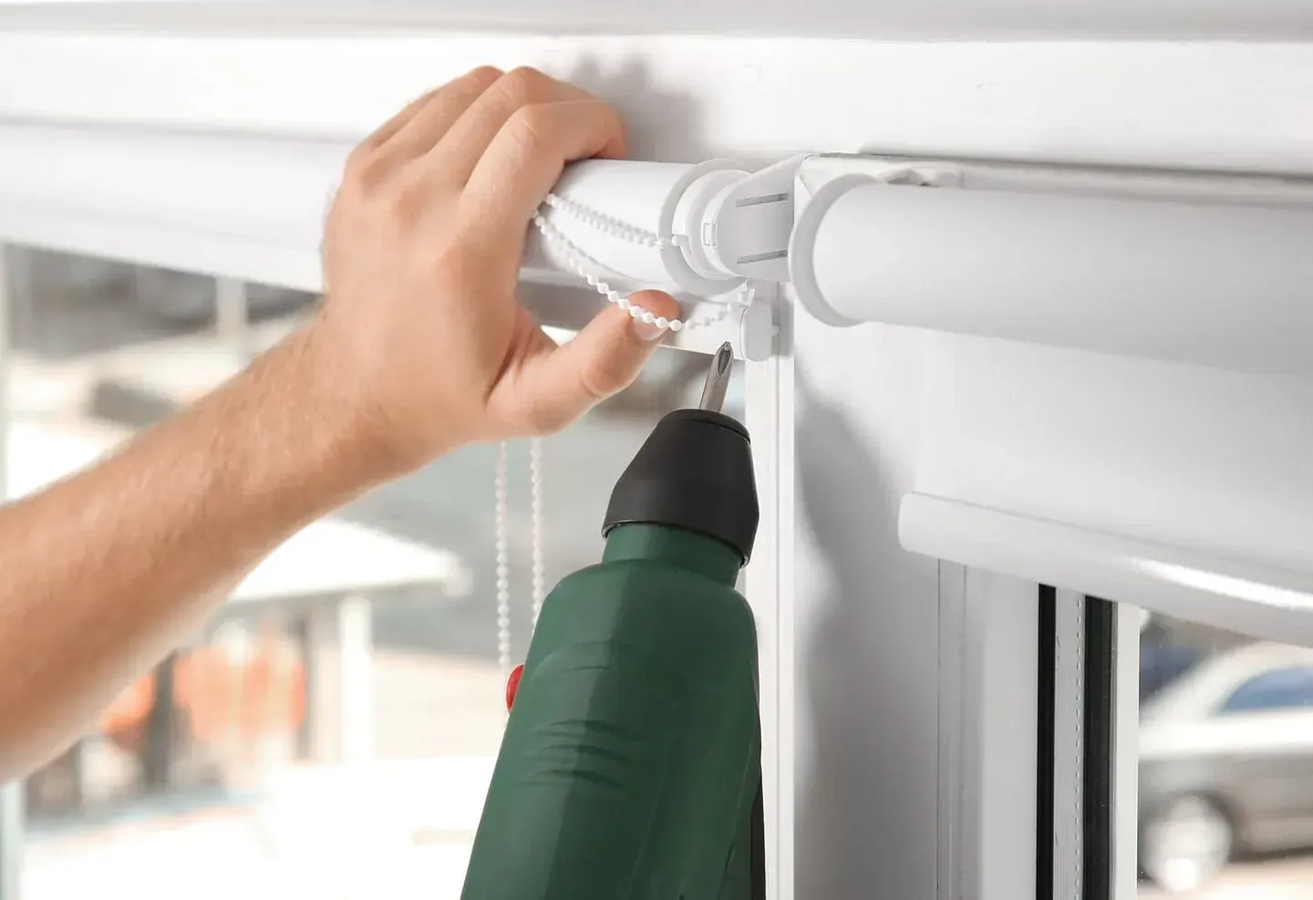 Una persona está instalando una persiana en una ventana con un taladro.