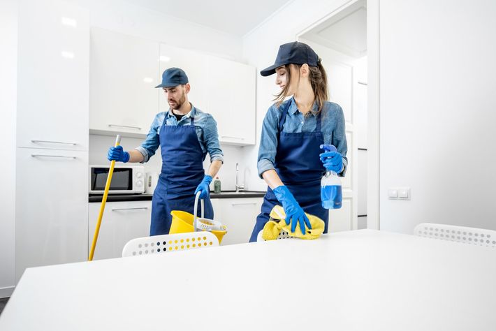 Una mujer está limpiando una mesa con una botella de spray y un paño.