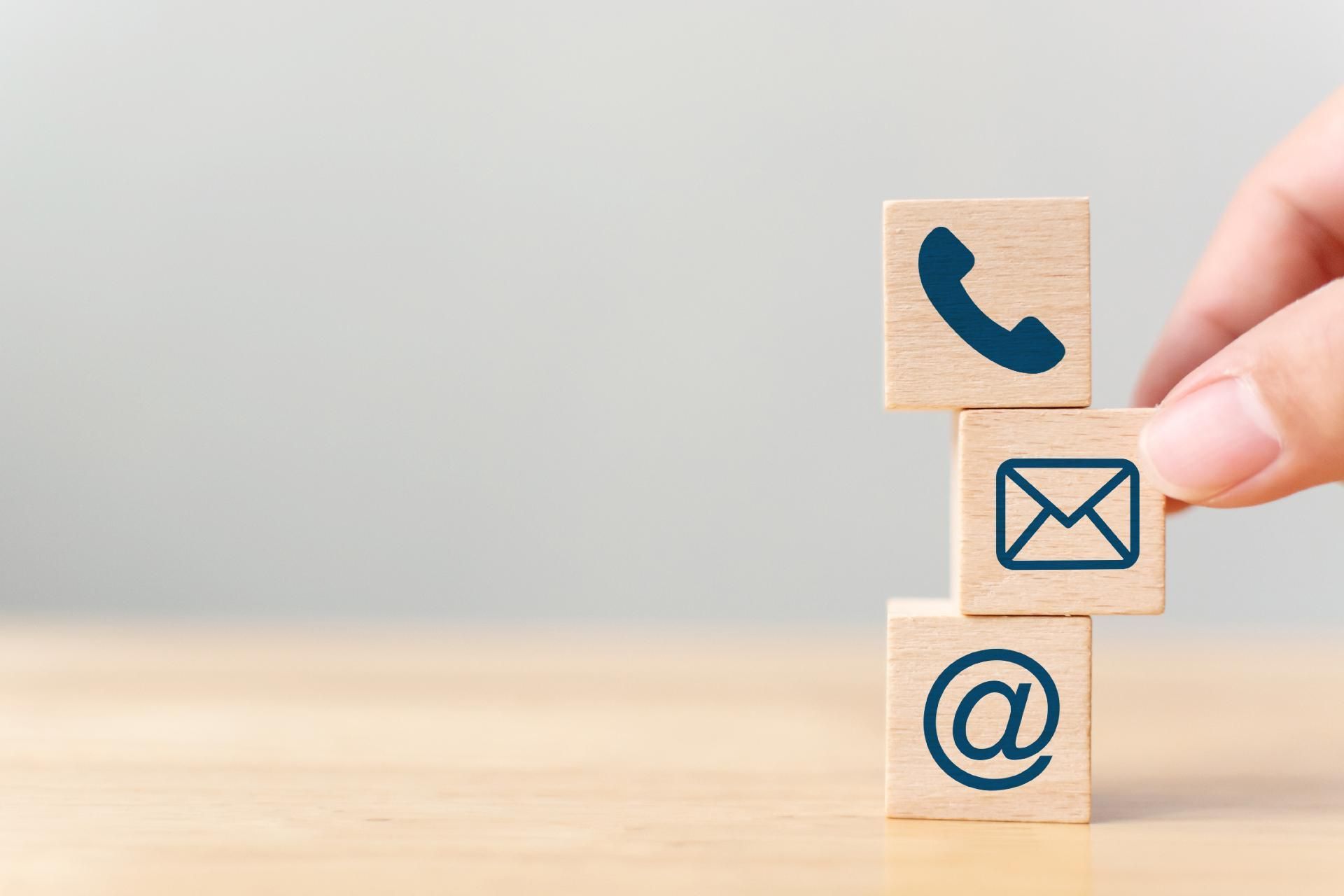 Helle Holzblöcke mit blauem Aufdruck mit Symbolen von einem Telefon, einem Briefumschlag und einem @-Symbol