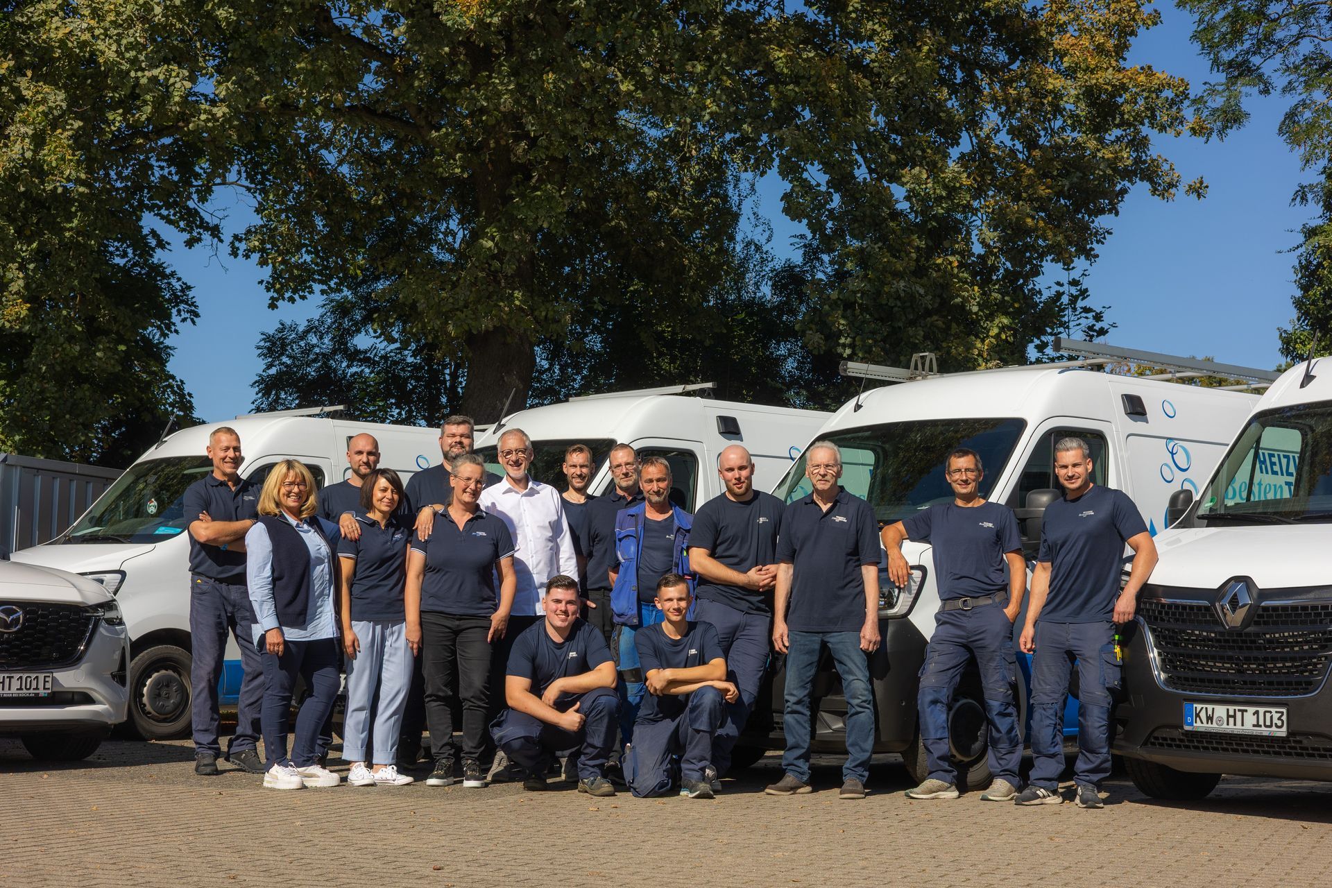 Eine Gruppe von Personen in einheitlicher Kleidung posiert mit einem Firmenwagen mit der Aufschrift „Heizungs Technik“.