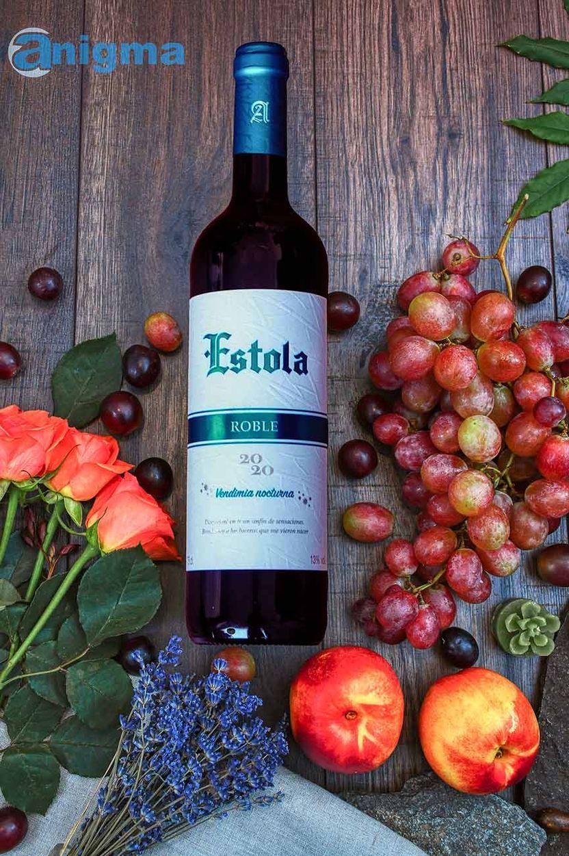 Una botella de vino de Estola está rodeada de frutas y flores.
