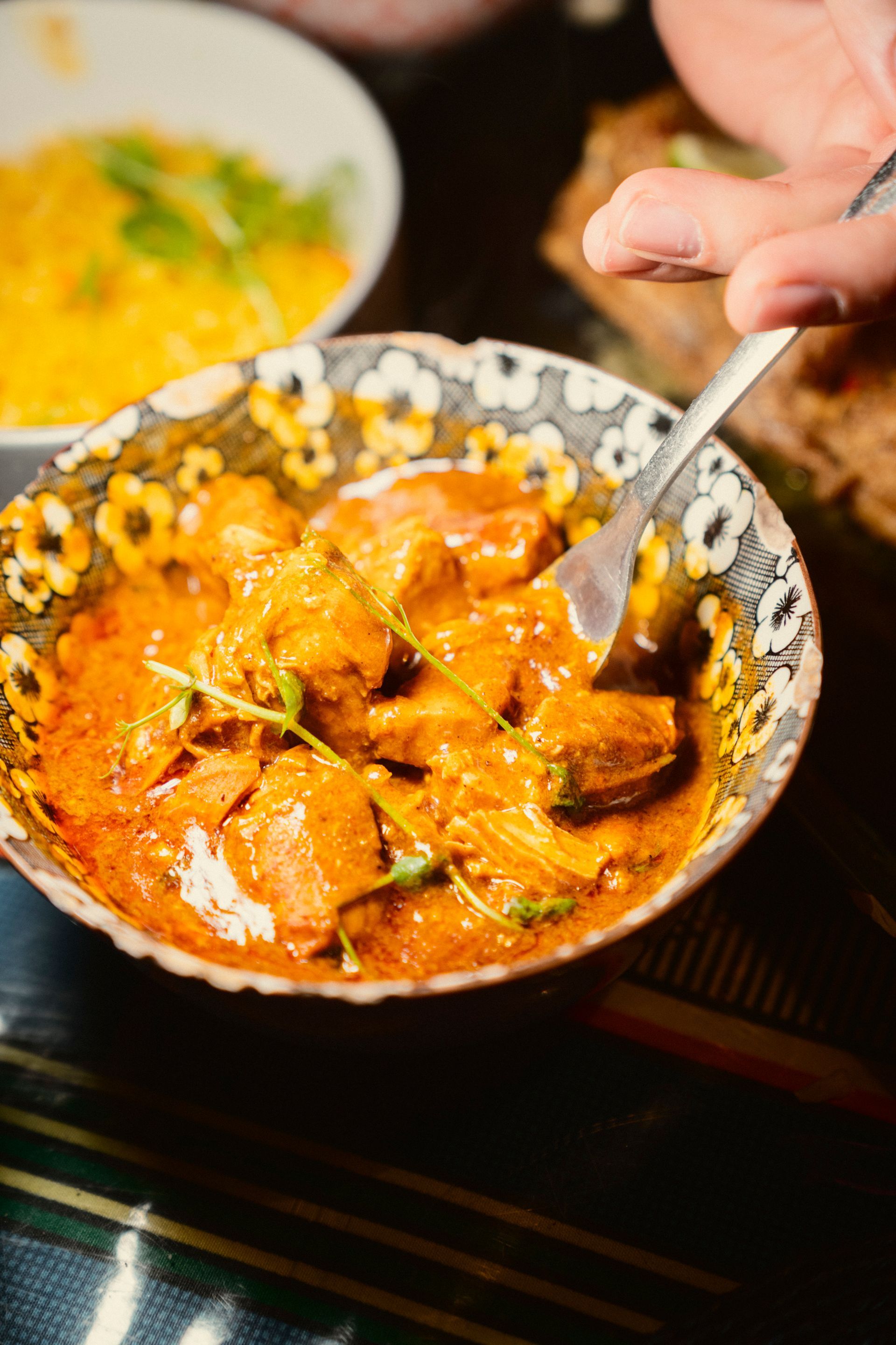 Eine schwarz weiß geblümte Schalte gefüllt mit orangenem Curry auf einem Holztisch mit einer Gabel darin