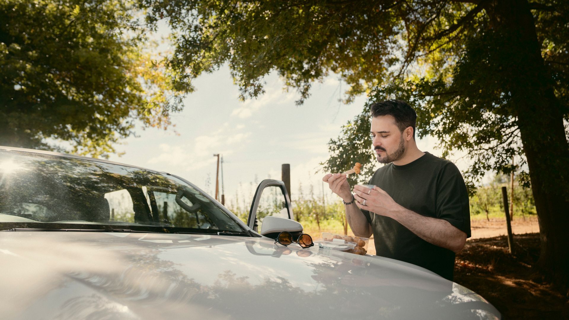 Pause am Straßenrand Mann isst einen Snack unter Bäumen und nutzt die Motorhaube als Tisch