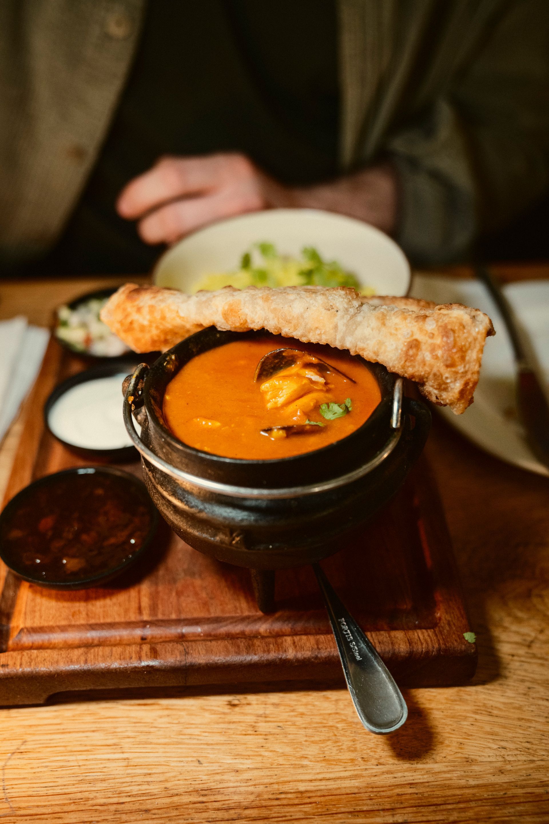 Schwarzer kleiner Top mit Curry auf dem ein kleiner aufgerollter Fladen liegt