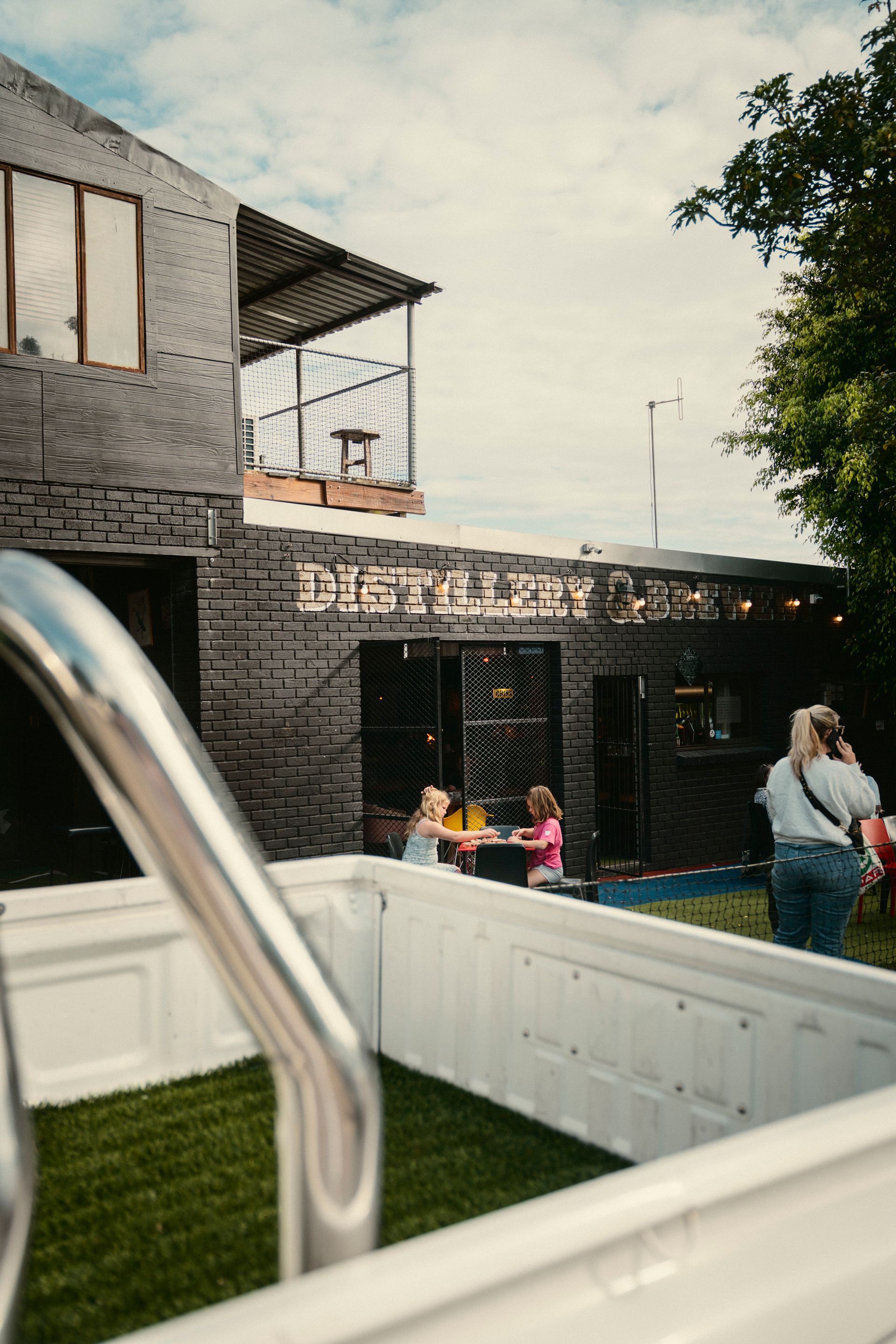 Blick auf Distillery mit spielenden Kindern und telefonierender Frau