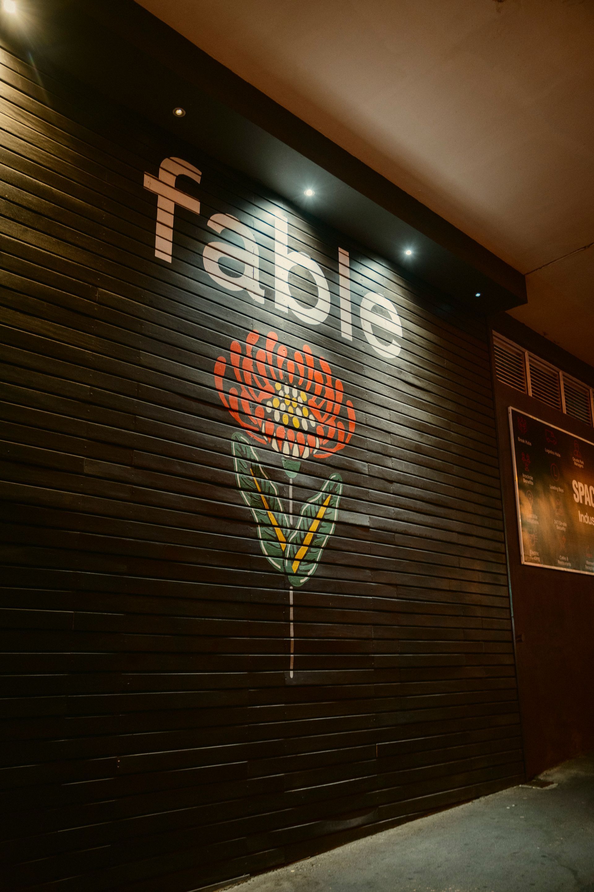 Fabel Bar Logo Mural auf einer schwarzen Holzwand. gezeichnete Protea Blume mit rotem Kelch und weißer Schrift