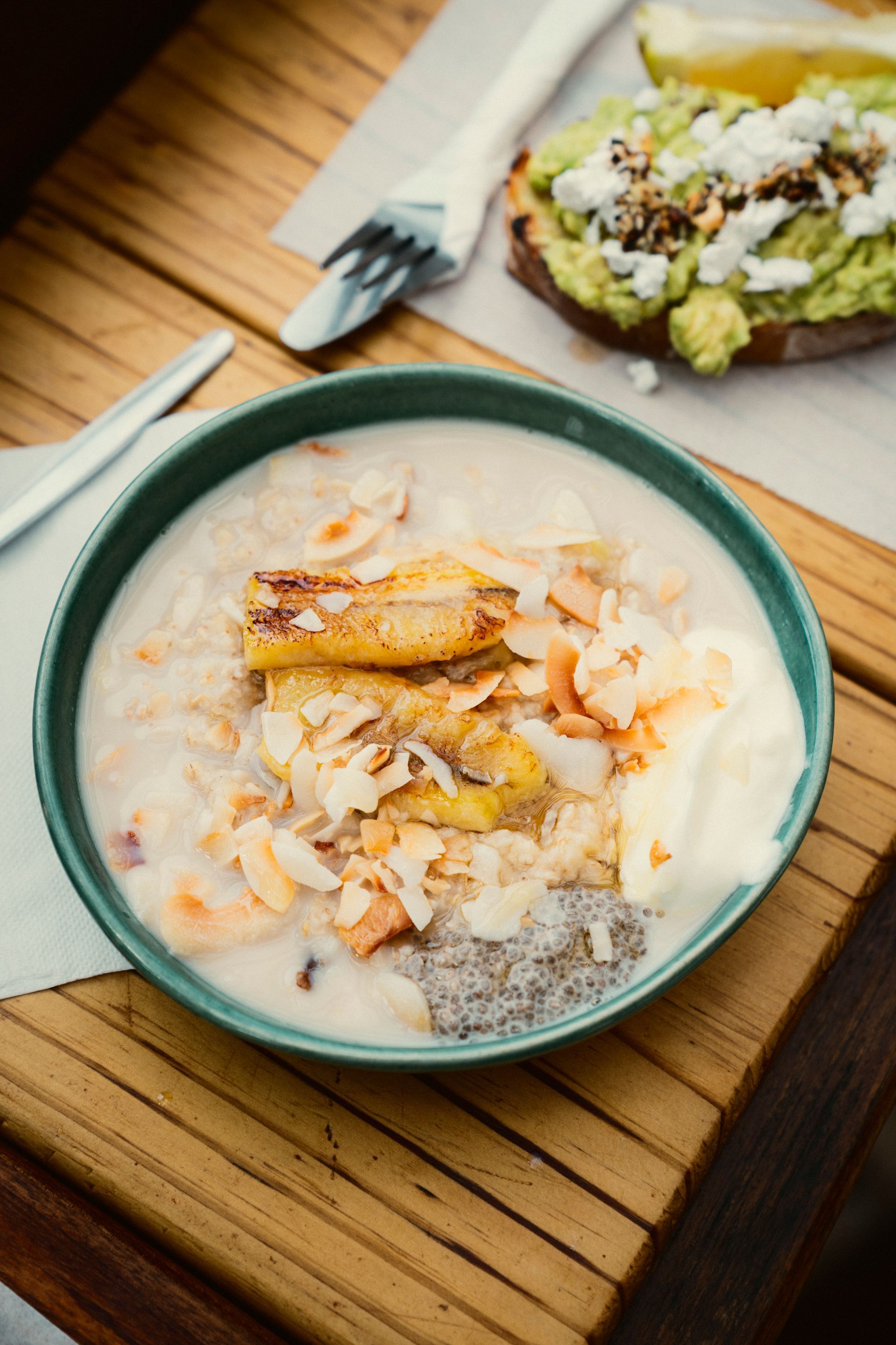 Holztisch mit Chiapudding, Banane und Avocado-Brot