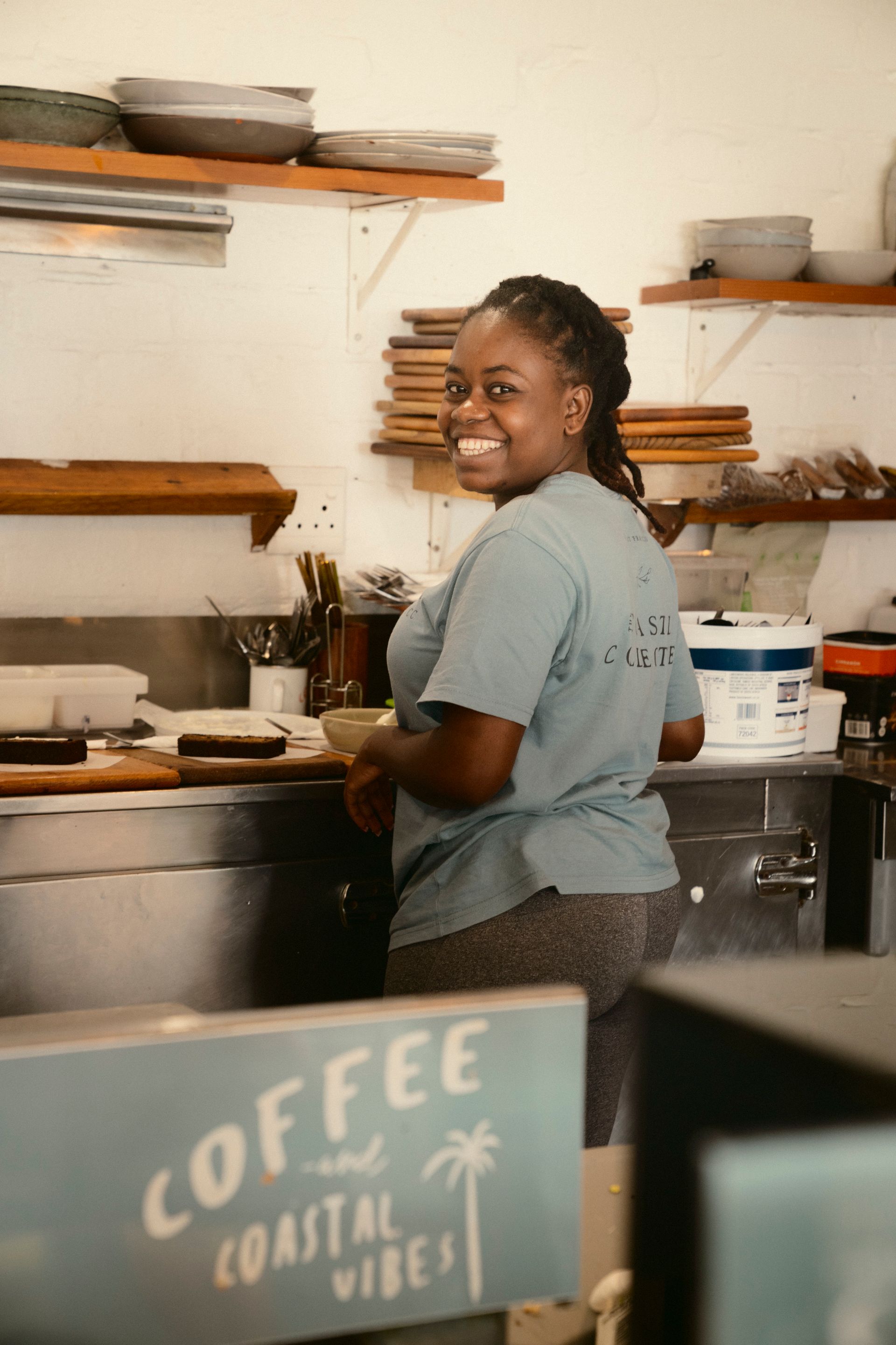 Barista im Coffee Shop vor Logo „COFFEE Coastal Vibes“