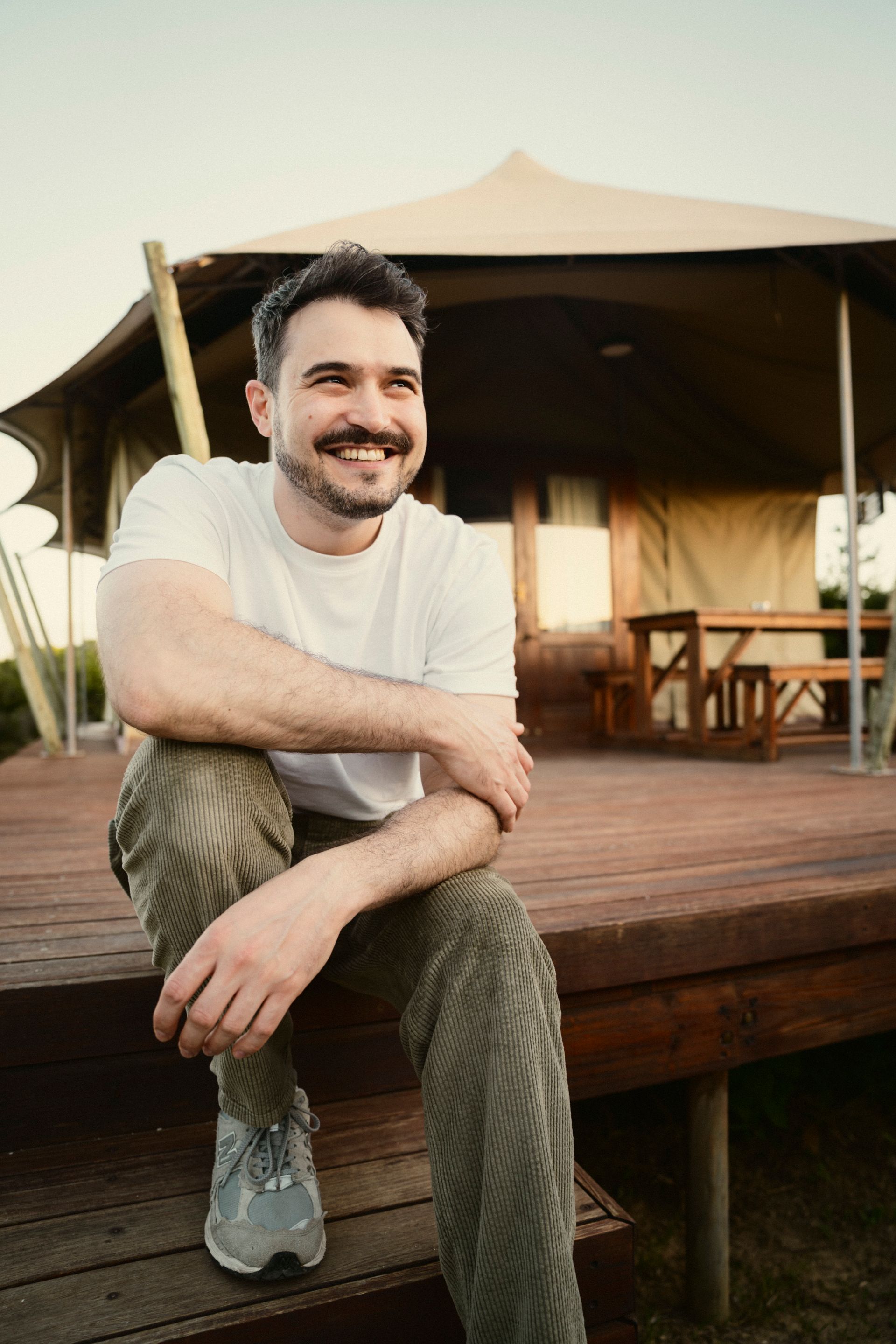 Markus sitzt vor einem Glamping Safari Zelt bei Abendstimmung und lacht