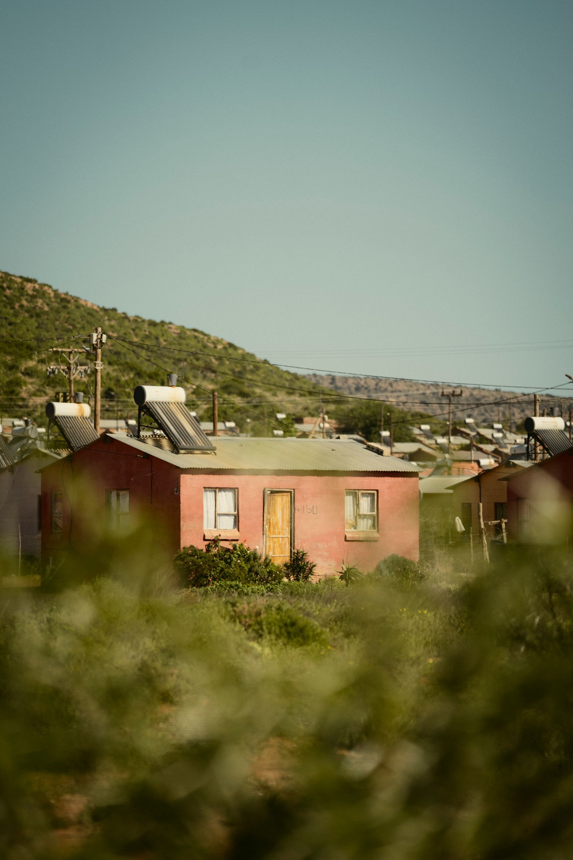 Ein rotes einfaches Haus einer afrikanische Siedlung mit grüner Vegetation im Vordergrund