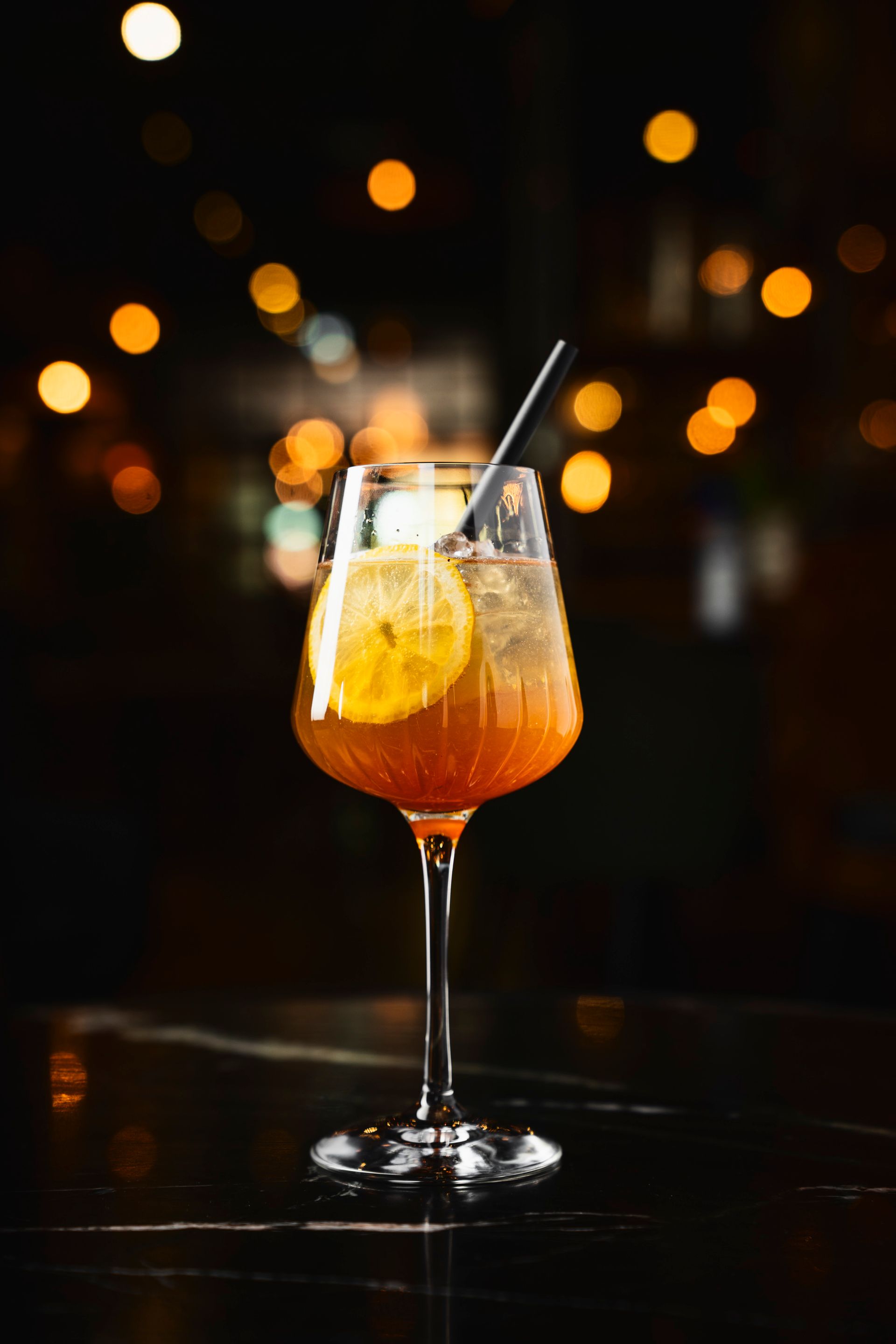 Foto vom ROOIBOS SPRITZ. Weinglas mit Eiswürfeln, Zitronenscheibe und schwarzem Strohhalm