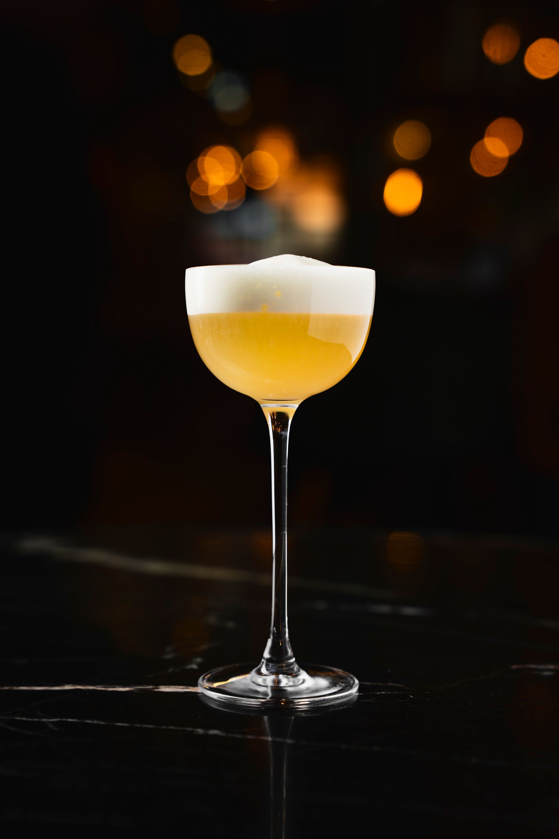 elegantes, langstieliges Cocktailglas mit dem MALVA Cocktail. Gelb mit cremiger Schaumkrone