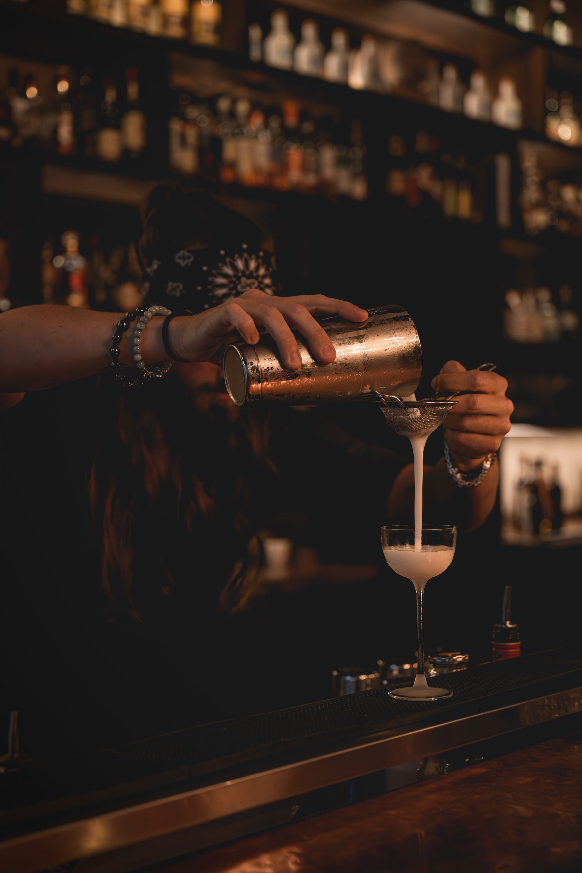 Ein Barkeeper gießt einen Cocktail aus einem Mixbecher durch ein Sieb in ein Cocktailglas.