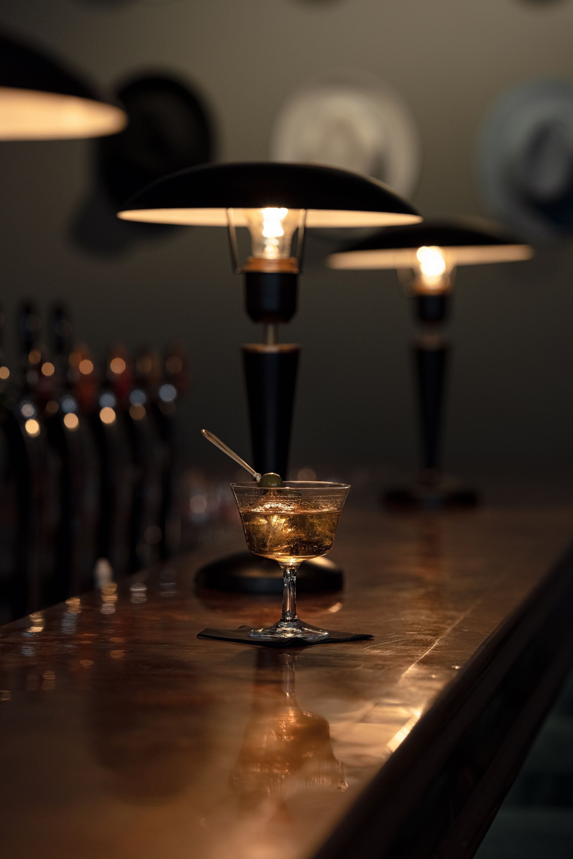 Cocktailglas auf Tresen der Three Fingers Bar mit Lampen