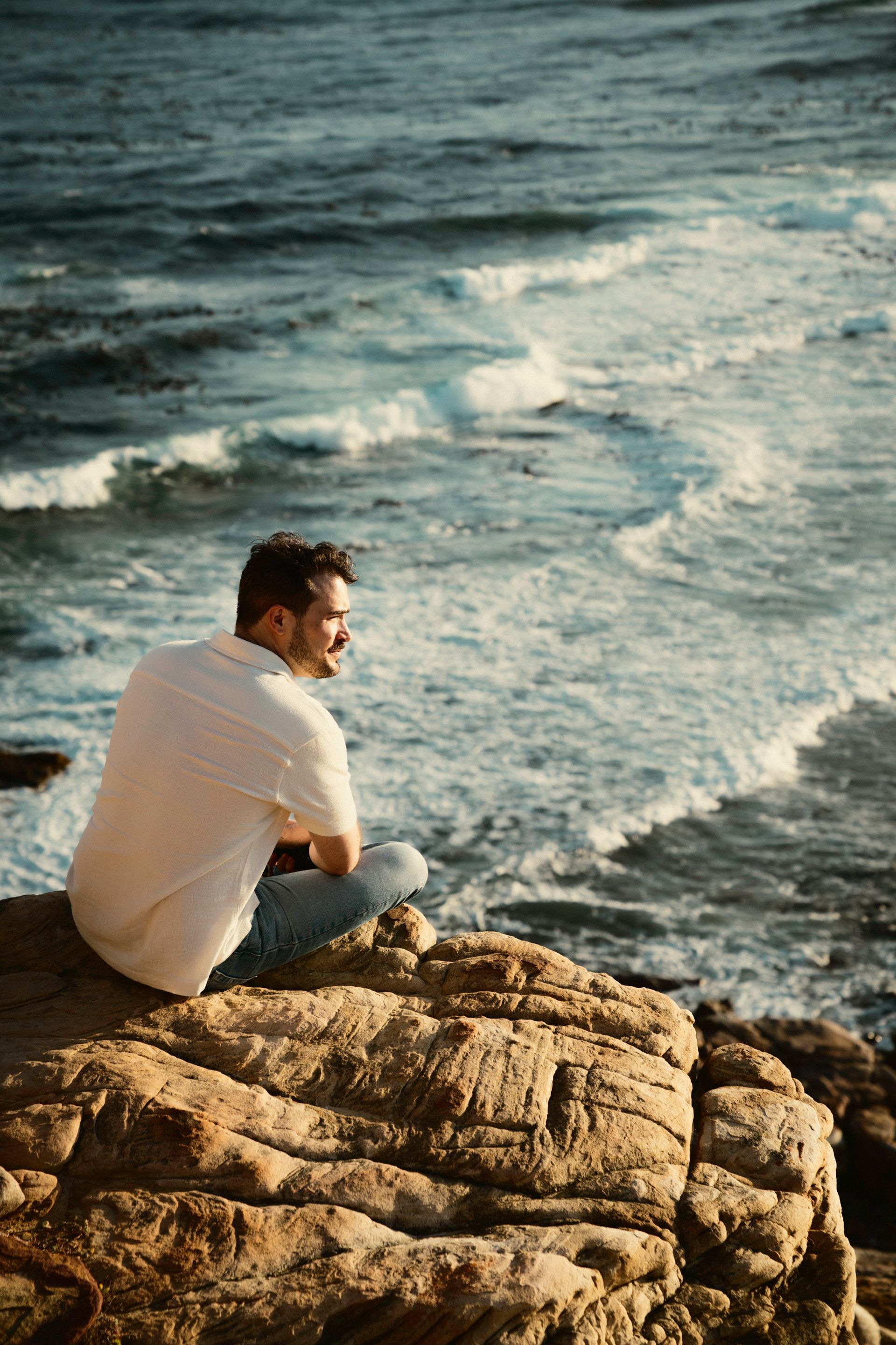 Markus sitzt auf einem Felsen und schaut auf das Meer herab