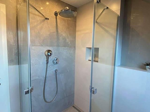 Ein Badezimmer mit ebenerdiger Dusche mit Glastür und Duschkopf.