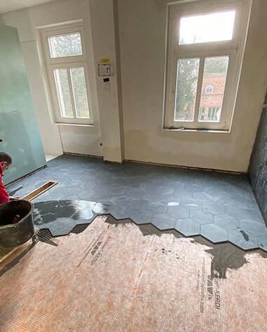 Eine Person verlegt Fliesen auf dem Boden eines Raumes.