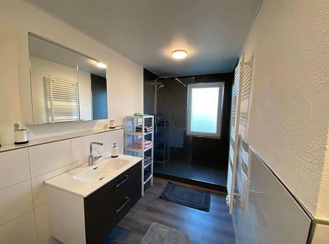 Ein Badezimmer mit Waschbecken, Spiegel und ebenerdiger Dusche.