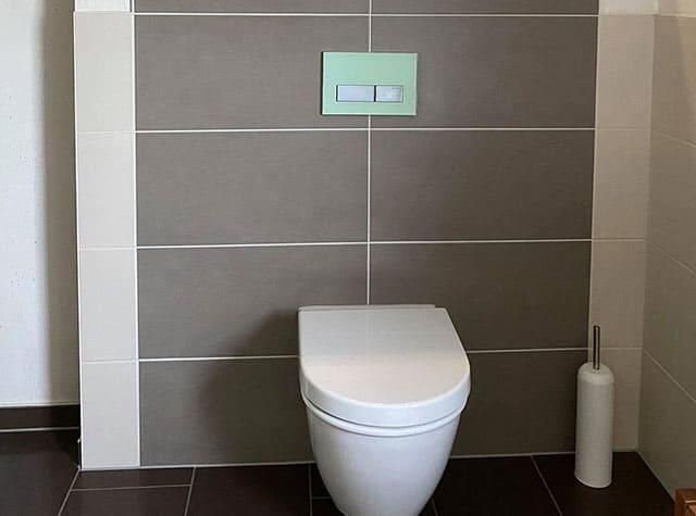 Eine weiße Toilette steht in einem Badezimmer neben einer Wand.
