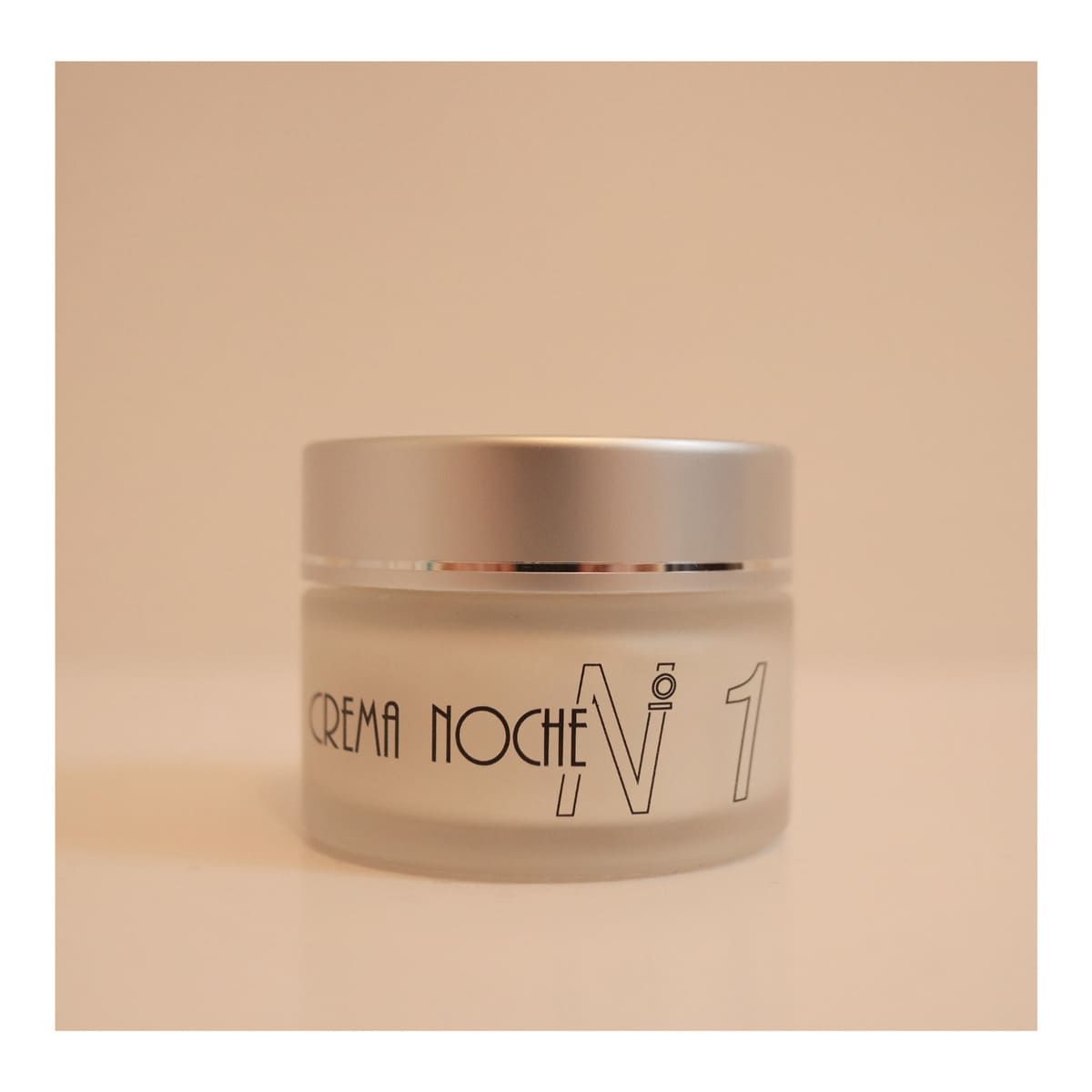 Tarro de crema de noche, de vidrio esmerilado con tapa plateada. Etiqueta con la inscripción 