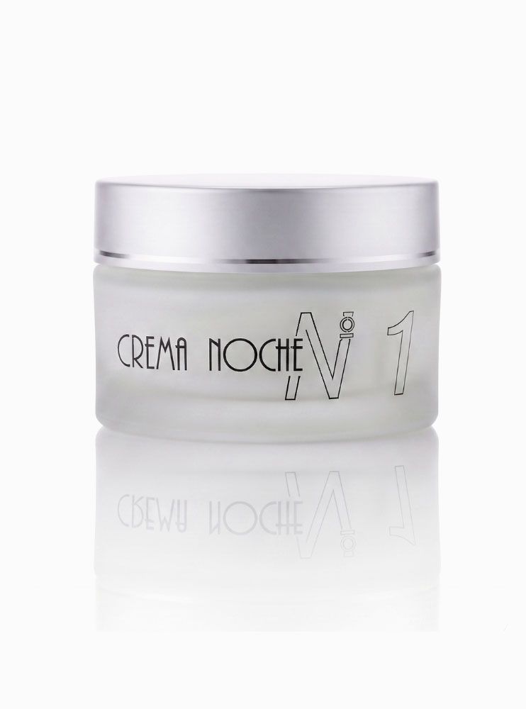 Tarro de cosméticos blanco con la etiqueta “Crema Noche” y tapa plateada sobre fondo blanco.