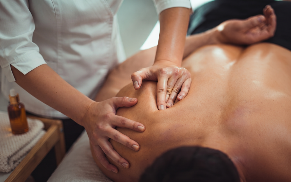 Masajista aplicando presión en la espalda de un cliente en un entorno de spa.
