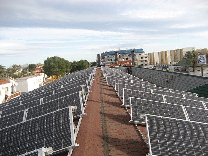 Hileras de paneles solares en una azotea que se extienden hasta el horizonte bajo un cielo parcialmente nublado.