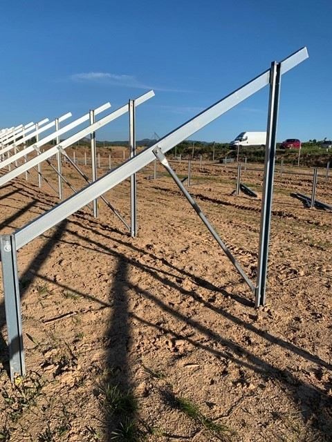 Hileras de estructuras metálicas blancas para paneles solares en un campo de tierra seca bajo un cielo azul despejado.