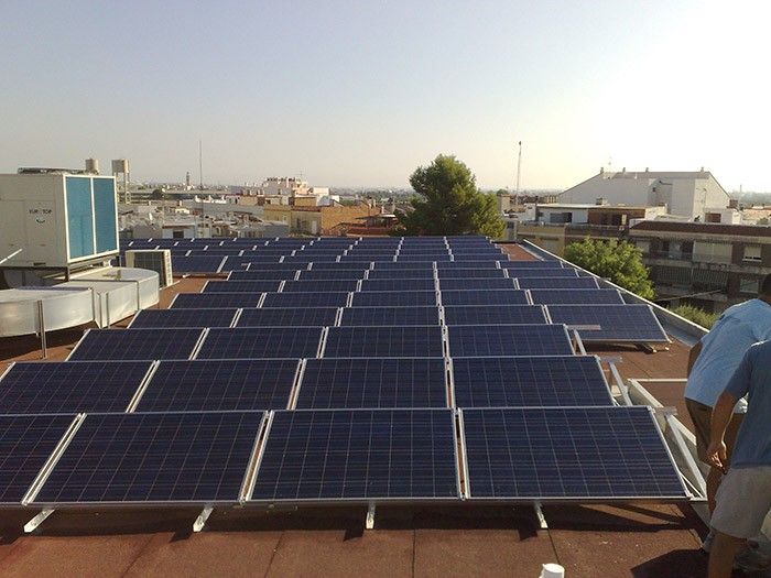 Paneles solares que cubren un tejado, con una persona de pie en el extremo derecho al fondo.