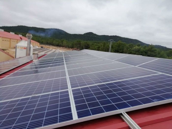 Paneles solares en un tejado con colinas verdes y cielo nublado al fondo.