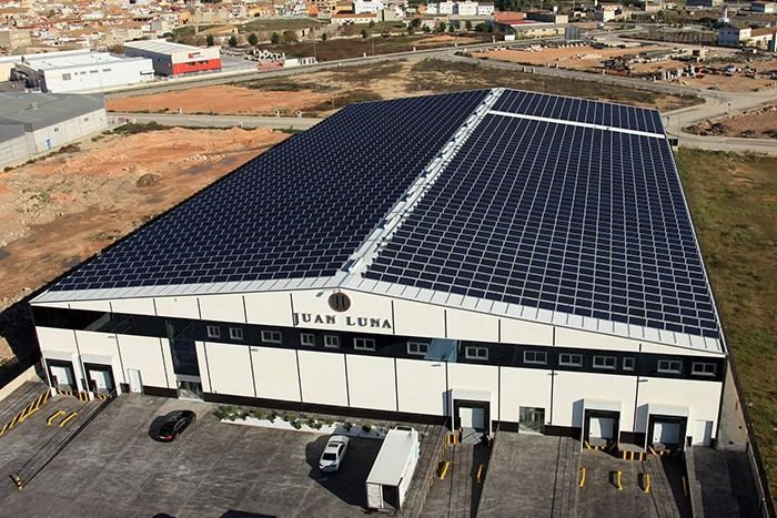 Vista aérea de un gran almacén con techo cubierto de paneles solares en una zona industrial.