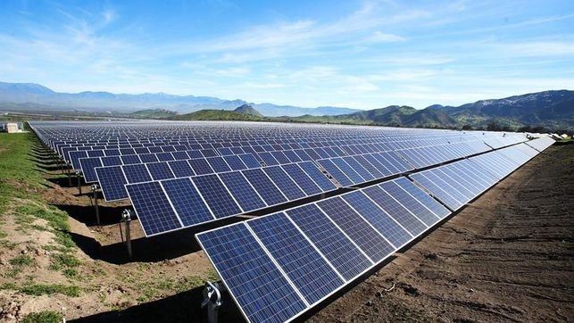 Conjunto de paneles solares en un campo bajo un cielo azul, con montañas al fondo.