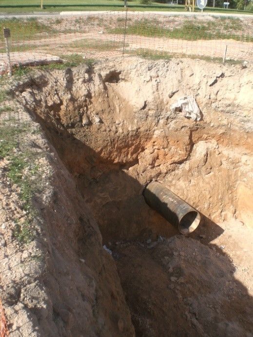 Gran excavación de tierra con una abertura para tubería de hormigón en la pared de la zanja, cerca de un campo de hierba.