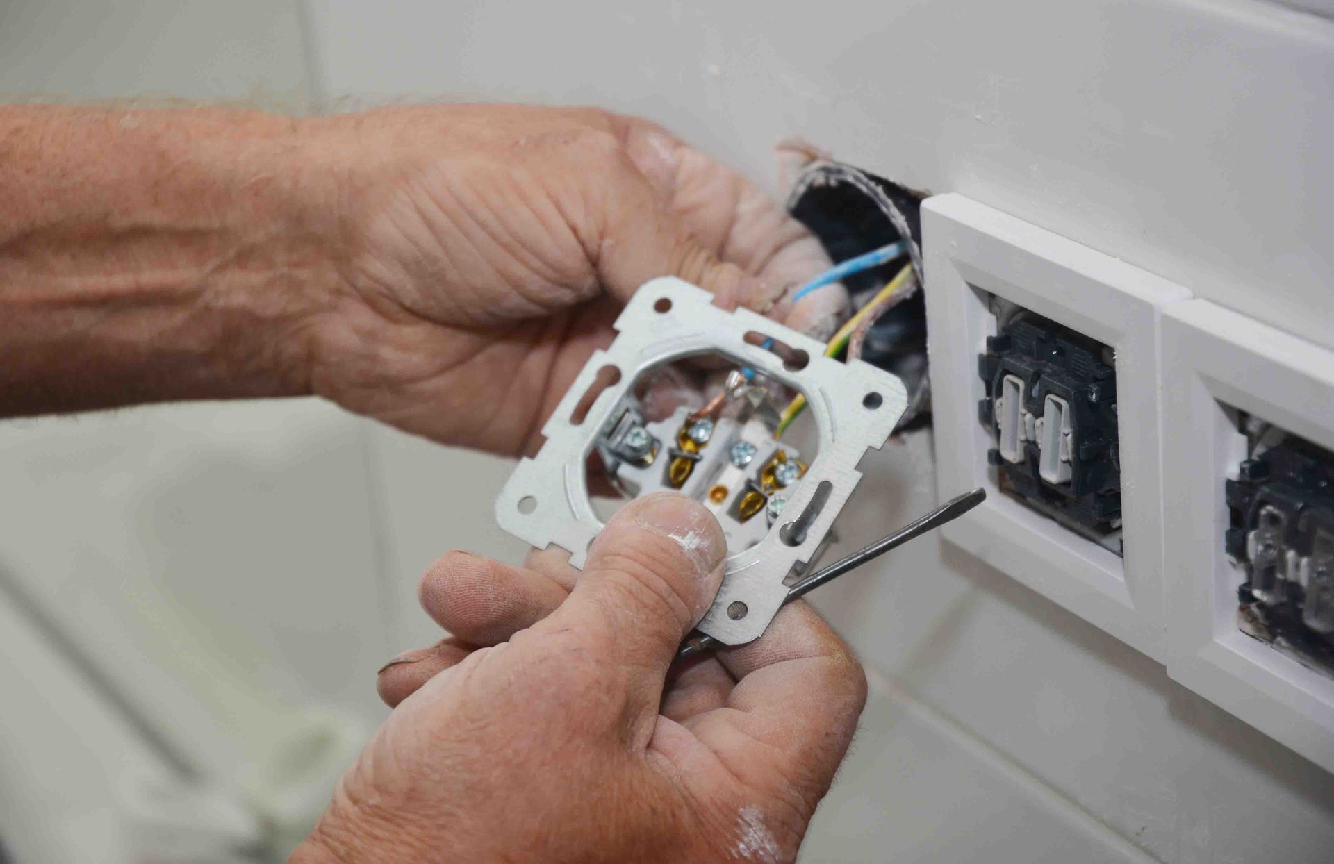 Manos cableando un tomacorriente de estilo europeo, con el tomacorriente parcialmente retirado de una pared blanca.
