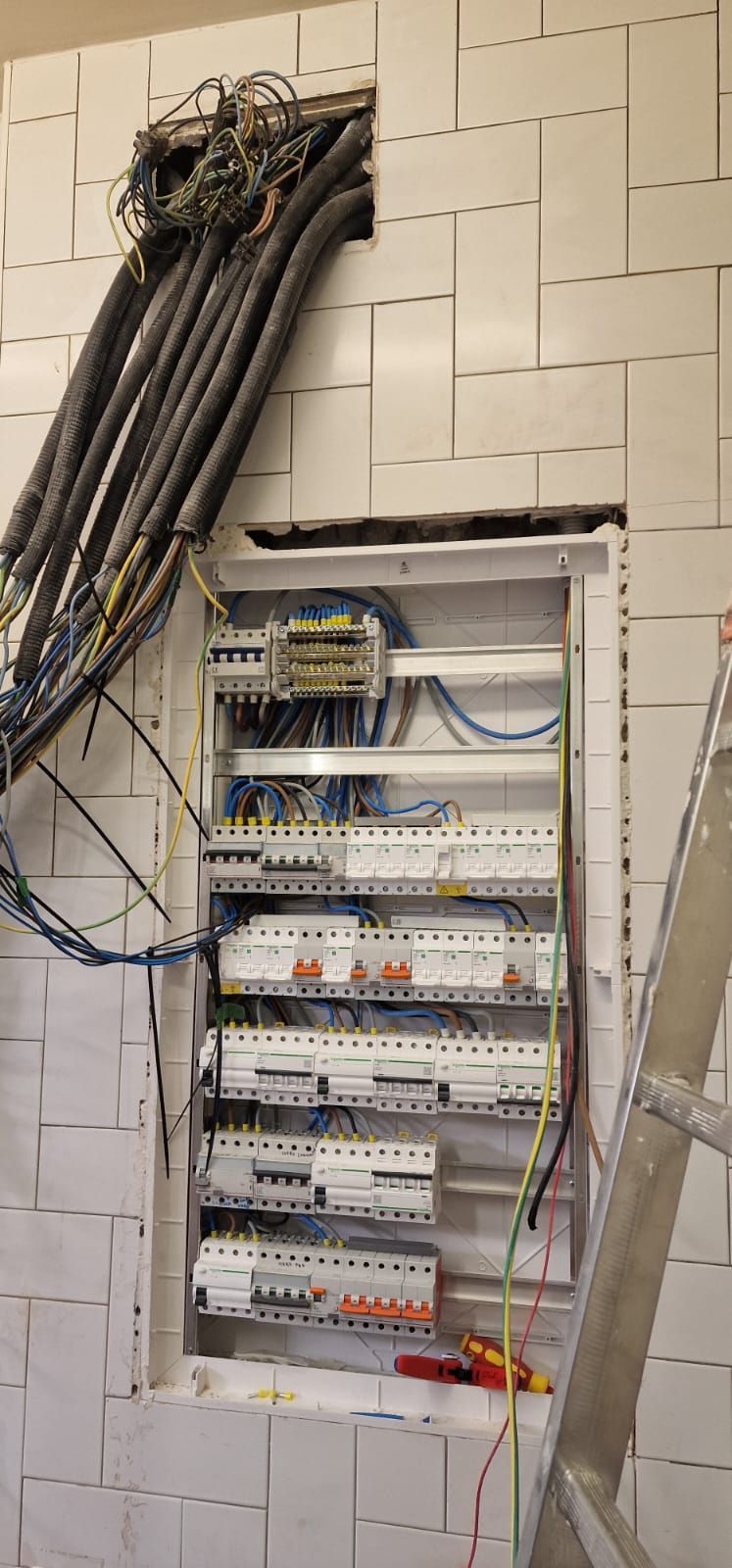 Hay un cuadro eléctrico instalado en una pared, con cables conectados. Hay una escalera a un lado.