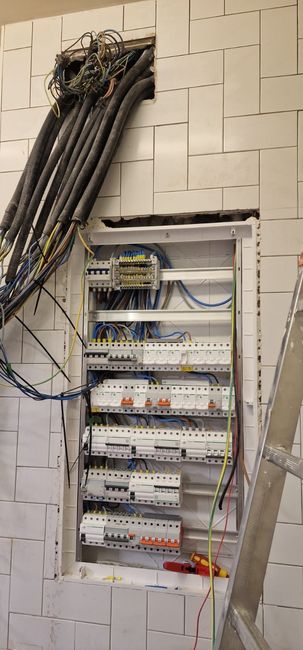 Hay un cuadro eléctrico instalado en una pared, con cables conectados. Hay una escalera a un lado.