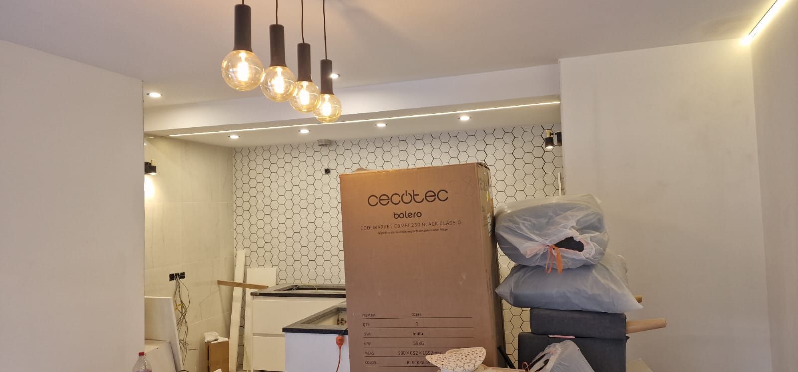 Fotografía interior con luces colgantes, una caja de cartón grande y artículos empacados, probablemente durante la renovación.