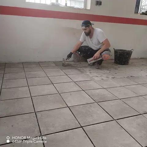 Un hombre está arrodillado sobre un suelo de baldosas con una paleta.