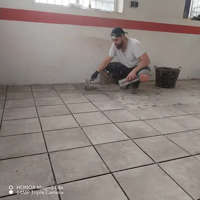 Un hombre está arrodillado sobre un suelo de baldosas con una paleta.