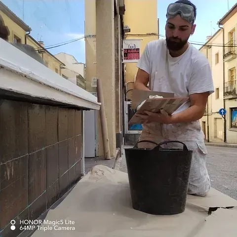 Un hombre que lleva gafas está arrodillado junto a un cubo negro.