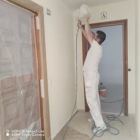 Un hombre está rociando pintura en una pared en un pasillo.