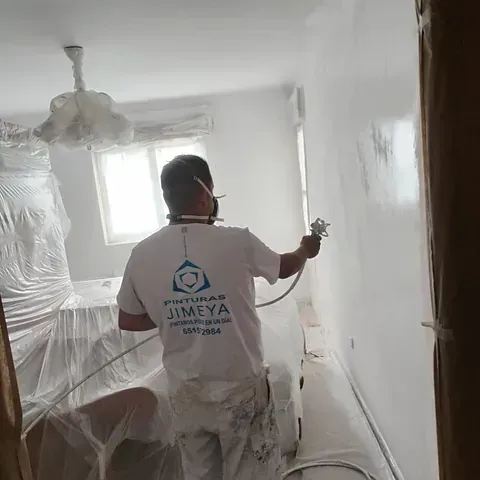 Un hombre está rociando pintura en una pared de una habitación.