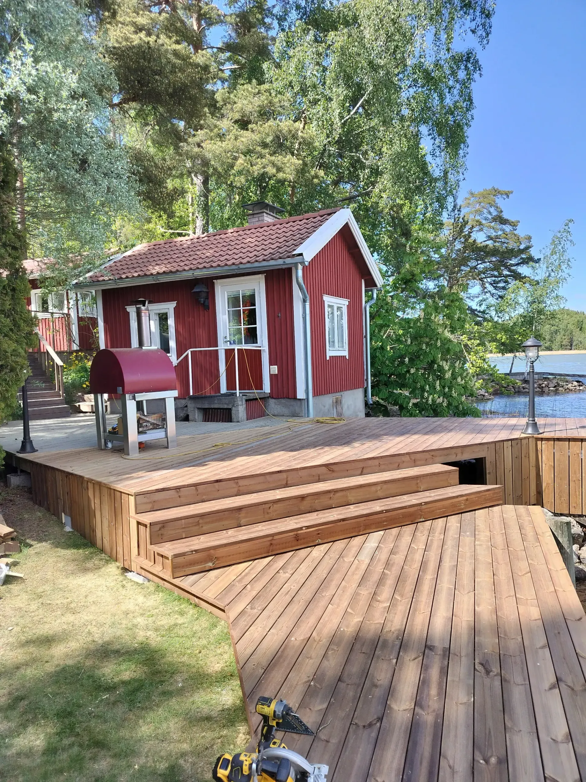 Punainen järvenrantamökki, jossa on terassi ja portaat puiden ja veden äärellä