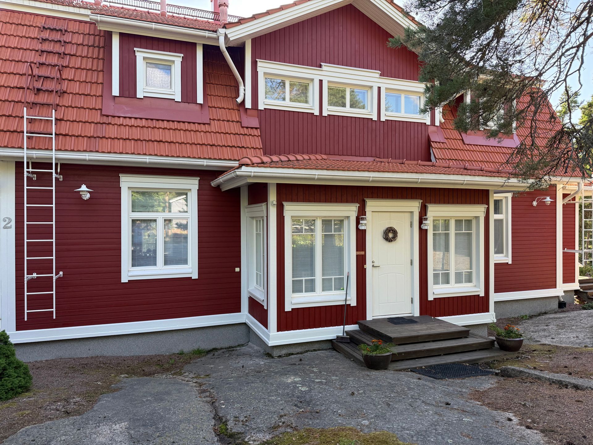 Punainen kaksikerroksinen talo, jossa on valkoiset reunukset, etuportaat ja sorapäällysteinen ajotie