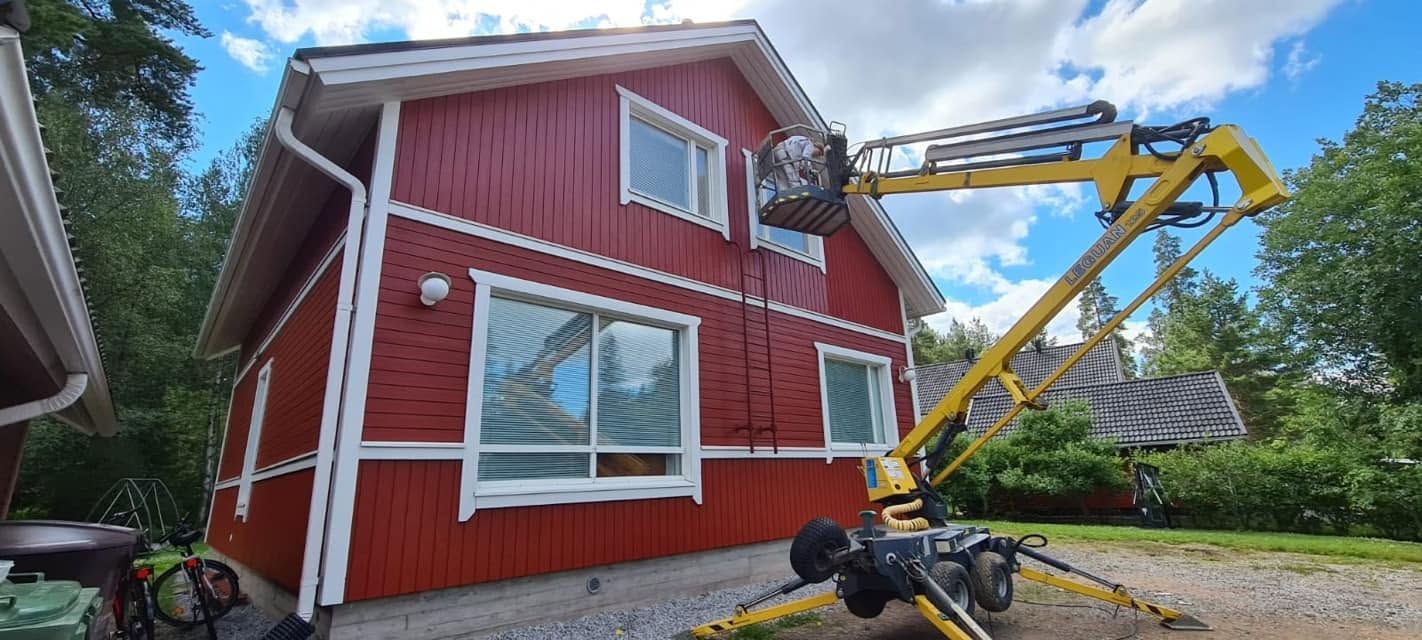 Hissityöntekijä maalaa kaksikerroksisen talon punaisen ulkopuolen.