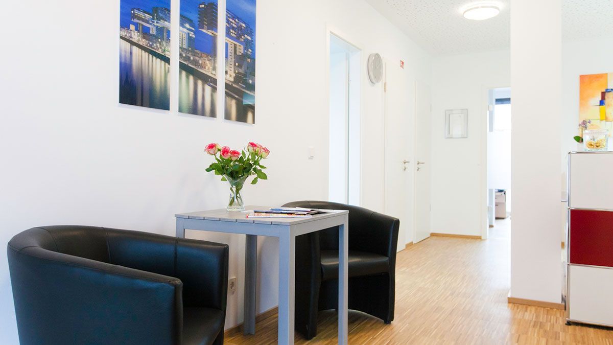 Ein Wartezimmer mit zwei Stühlen und einem Tisch mit einer Vase mit Blumen darauf.