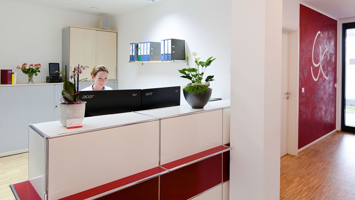 Eine Frau sitzt an einem Schreibtisch in einem Empfangsbereich.